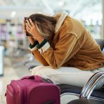 femme tenant sa tête avec ses deux mains est assise près de sa valise à l'aéroport